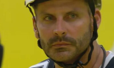 Close-up do rosto de Henri Castelli usando capacete, barba, olhos claros, fundo amarelo.