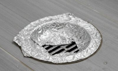 Papel alumínio amassado sobre ralo de chão com grades pretas e gotas d'água.