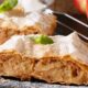 Duas porções de strudel de maçã com açúcar de confeiteiro, hortelã, maçãs vermelhas e peneira.