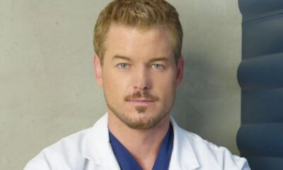 Retrato de Eric Dane, com cabelo loiro, barba, jaleco branco e scrub azul.