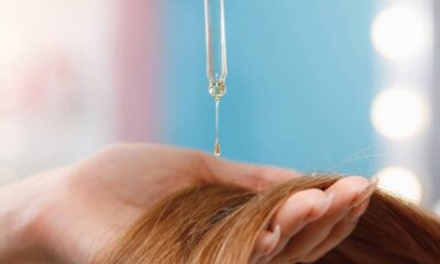 Mão aplica gotas de óleo dourado com conta-gotas em cabelos castanhos claros.