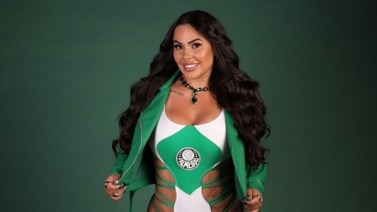Mulher sorridente, cabelos longos e escuros, jaqueta verde e body branco e verde com logo do Palmeiras.