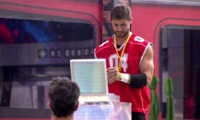 Jonas Sulzbach de camisa '04' vermelha, com medalha, segura objeto iluminado.