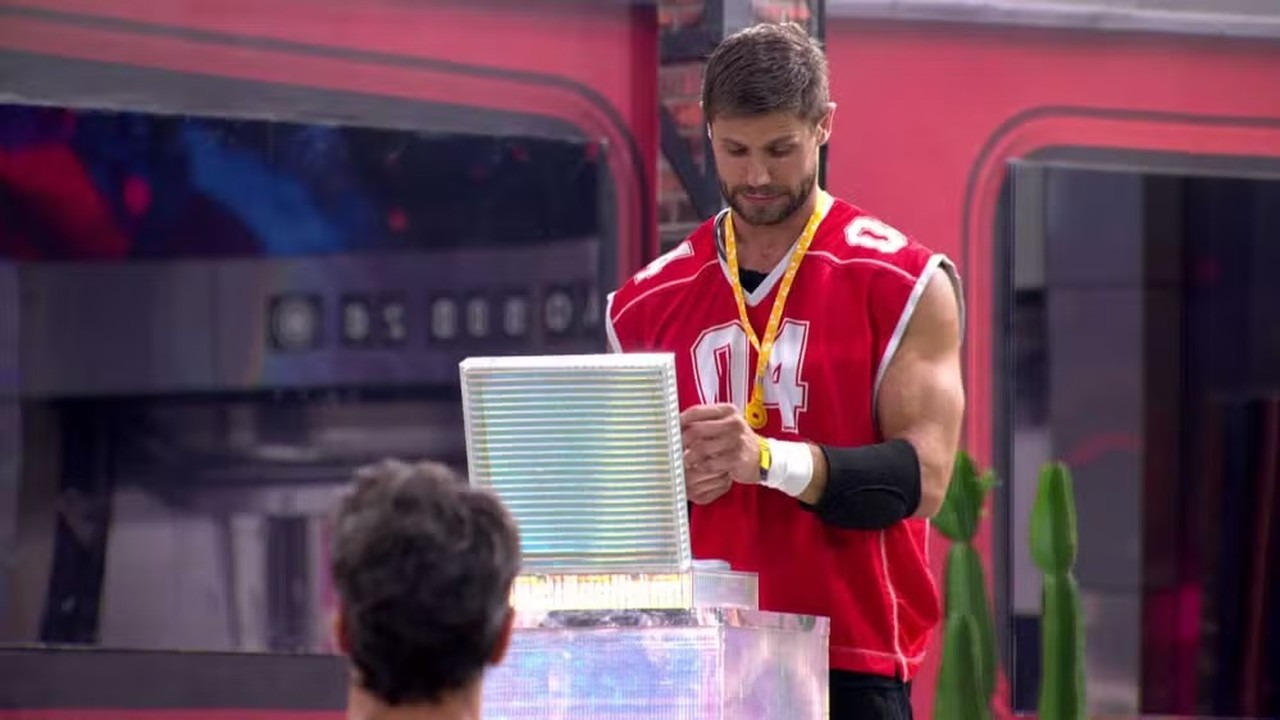 Jonas Sulzbach de camisa '04' vermelha, com medalha, segura objeto iluminado.