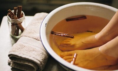 Pés de molho em uma bacia com água e canela em pau, ao lado de toalha e jarra.