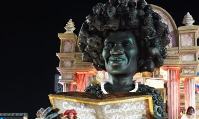 Escultura gigante de mulher negra sorrindo em carro alegórico com livro aberto, Carolina Maria.