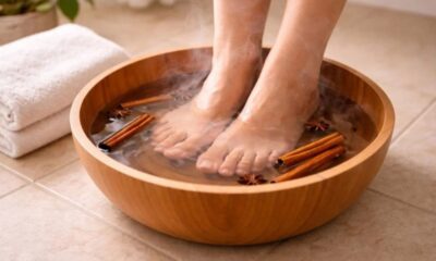 Pés de uma pessoa em bacia de madeira com água quente, canela e anis estrelado.