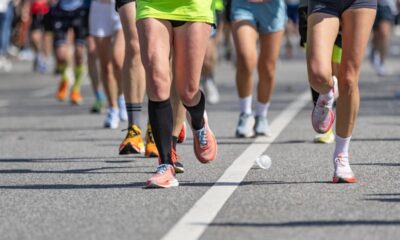 Pernas de corredores em movimento durante uma maratona, com tênis e um copo descartável no asfalto.