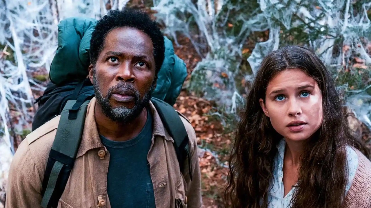 Duas pessoas em floresta coberta por teias, um homem e uma mulher, olham para cima.