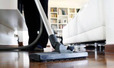 Base de aspirador de pó no chão de madeira, com pessoa aspirando a sala.