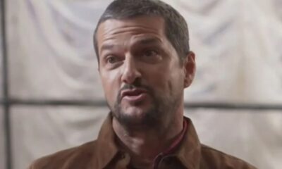 Marcelo Serrado, homem de meia-idade com barba, jaqueta marrom, olhando e falando.