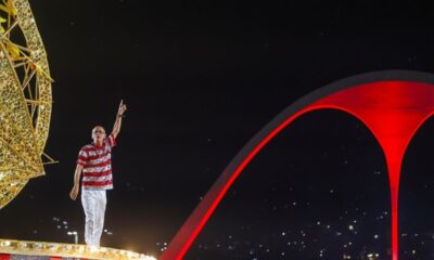 Mestre Ciça em carro alegórico, com camisa listrada, apontando para cima na Sapucaí.