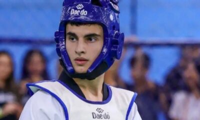 Jovem atleta de taekwondo, usando capacete e colete azul e branco com logo Daedo.