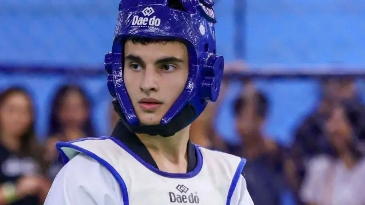 Jovem atleta de taekwondo, usando capacete e colete azul e branco com logo Daedo.