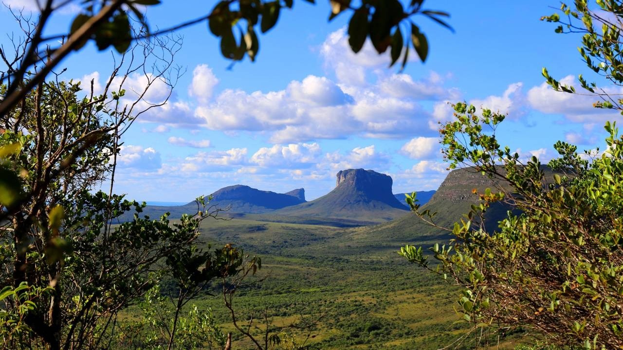 Vista panorâmica de montanhas de topo plano e vales verdes sob céu azul com nuvens.
