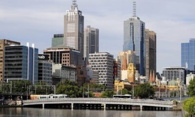 Paisagem urbana de Melbourne com arranha-céus, rio, ponte com bonde e veículos.