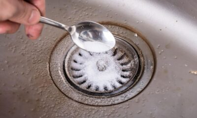 Mão despeja pó branco de colher em ralo de pia de metal.