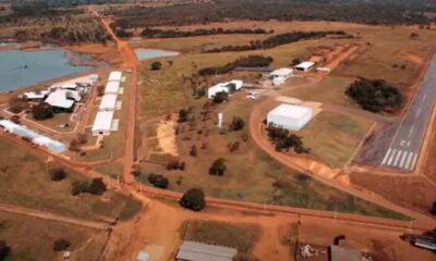 Vista aérea de uma grande fazenda com pista de pouso, edifícios brancos, lago e estradas de terra.