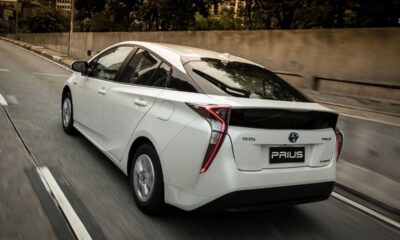 Toyota Prius branco híbrido em movimento em uma estrada urbana, visto por trás.