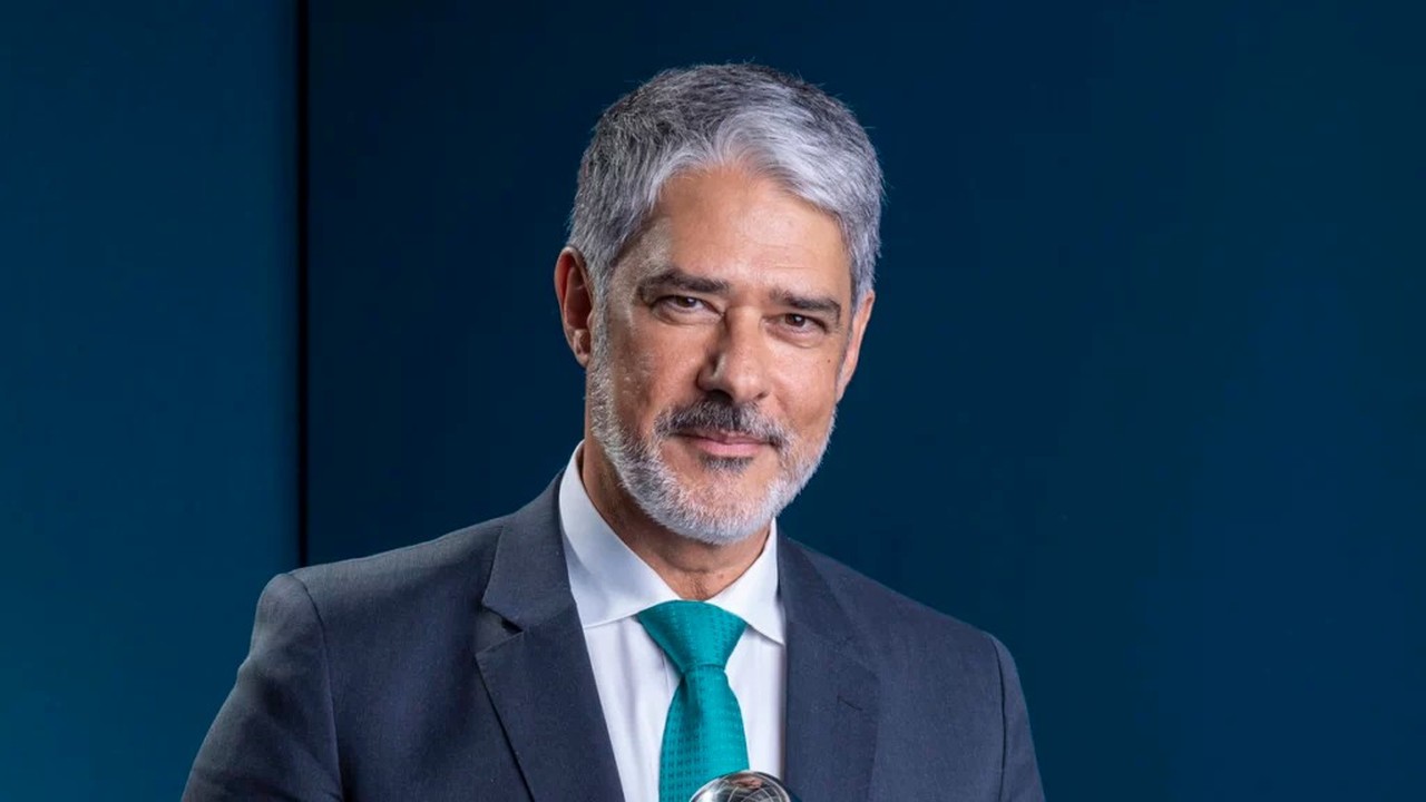 William Bonner, homem de cabelos grisalhos e barba, terno escuro e gravata azul-petróleo, olhando para frente.