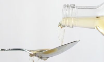 Vinagre transparente sendo despejado de uma garrafa de vidro em uma colher de metal.