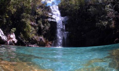 Cachoeira exuberante com água cristalina em tons de azul, cercada por mata verde e rochas.