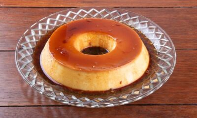 Pudim de leite com calda de caramelo em prato de vidro sobre mesa de madeira.