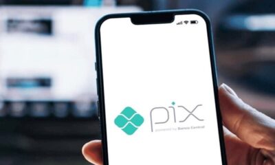 Mão segura celular com o logo do Pix e texto 'powered by Banco Central' na tela.