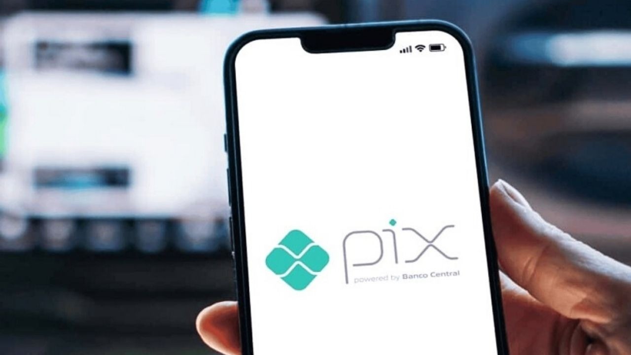 Mão segura celular com o logo do Pix e texto 'powered by Banco Central' na tela.