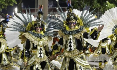 Duas pessoas sorridentes em fantasias pretas, brancas e douradas de Carnaval com pintura facial.