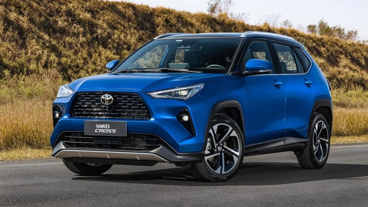 SUV Toyota Yaris Cross azul com teto preto em estrada, com paisagem seca e vegetação ao fundo.