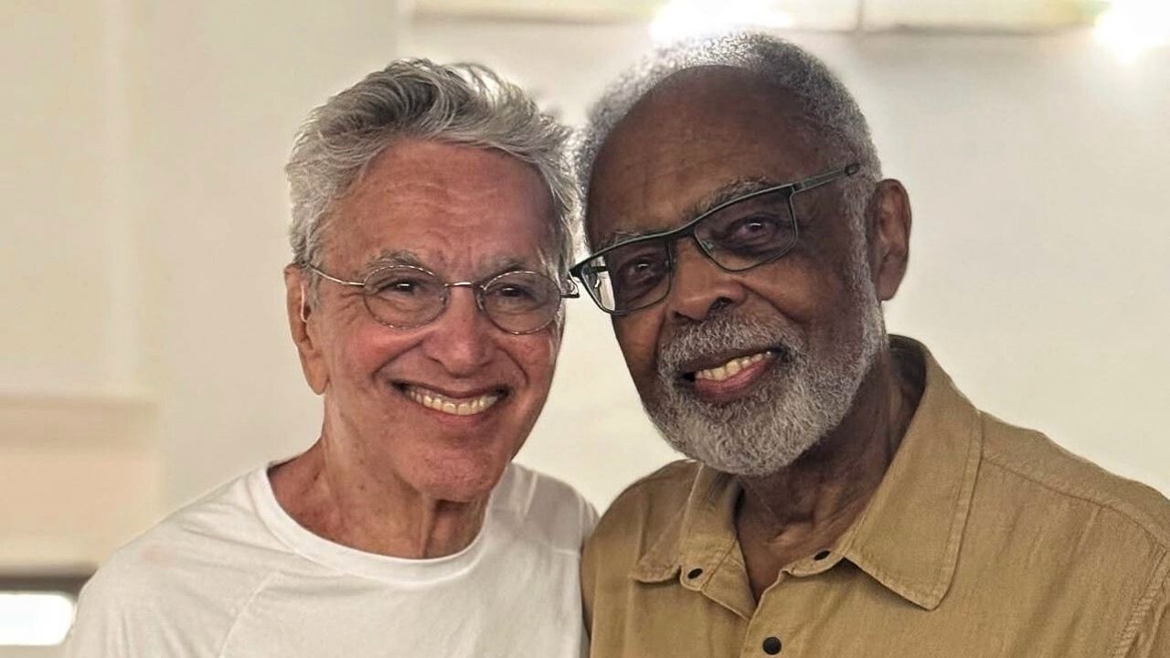 Caetano Veloso e Gilberto Gil, sorrindo, usando óculos, lado a lado.