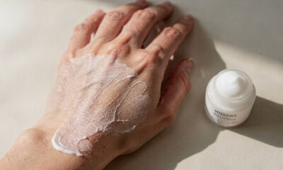 Mão borrifando solução de vinagre diluído na faixa do piso junto à porta de entrada, capacho ao lado e luz natural entrando pela porta, ambiente organizado e limpo, mostrando cuidado simples que melhora a sensação de casa limpa logo na chegada