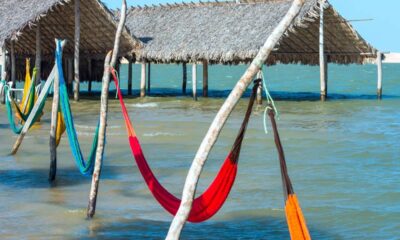 Redes coloridas suspensas sobre a água em um lago, com cabanas de palha no fundo.