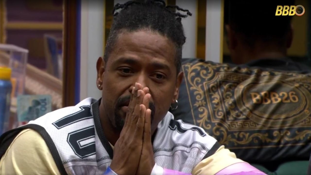 Homem de dreads com as mãos juntas, vestindo camisa de basquete número 10.