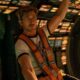 Ryan Gosling em um cockpit de nave espacial, com cinto de segurança laranja e óculos.