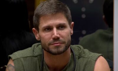 Jonas Sulzbach, com barba, usando blusa verde, olhando pensativo em ambiente escuro.