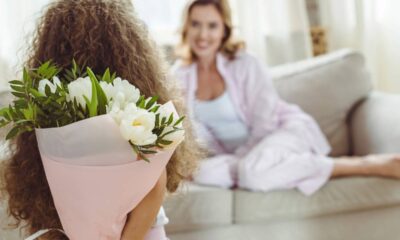 Menina de costas segura buquê de flores brancas para mulher sorridente em sofá.