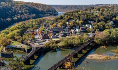 Vista aérea de uma cidade em vale arborizado com rio e pontes ferroviárias.