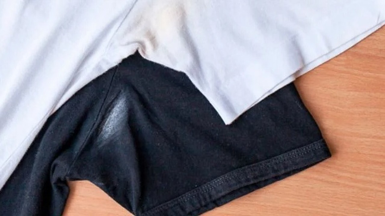 Camiseta branca com mancha amarela e camiseta preta com mancha branca de desodorante sobre madeira.