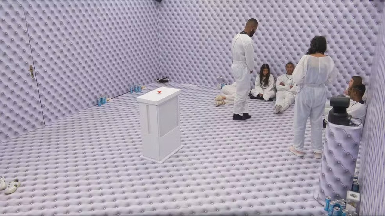 Confinados em quarto todo branco e acolchoado no BBB, com botão vermelho e latas azuis no chão.