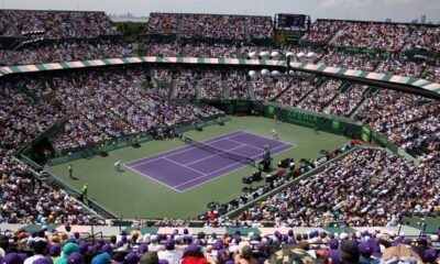Vista panorâmica do estádio lotado do Miami Open, com quadra de tênis roxa e dois jogadores.