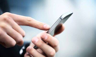 Mãos seguram um smartphone cinza e tocam a tela com o dedo indicador.