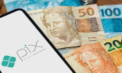 Tela de celular com logo Pix sobre notas de reais e moedas brasileiras.