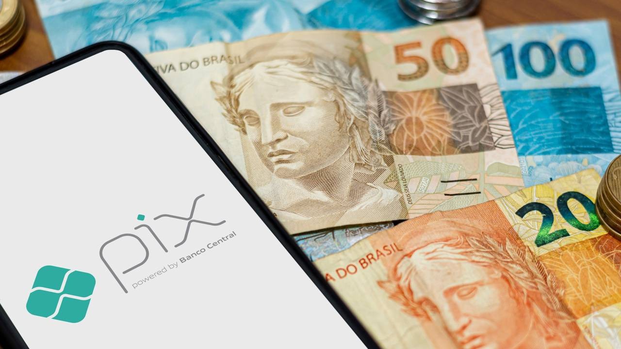 Tela de celular com logo Pix sobre notas de reais e moedas brasileiras.