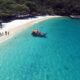 Vista aérea de praia com areia branca, mar turquesa cristalino, barco e pessoas em Arraial do Cabo.