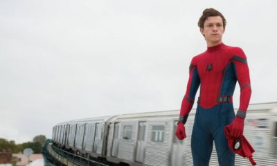 Tom Holland em traje de Homem-Aranha, sem máscara, próximo a um trem em movimento.