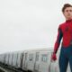 Tom Holland em traje de Homem-Aranha, sem máscara, próximo a um trem em movimento.