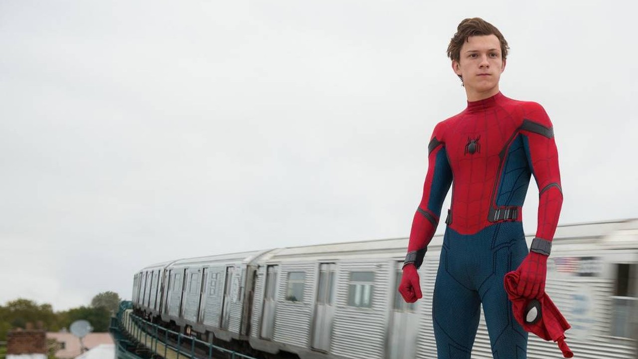 Tom Holland em traje de Homem-Aranha, sem máscara, próximo a um trem em movimento.