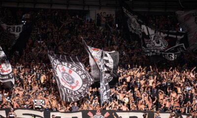 Multidão de torcedores do Corinthians em arquibancada, agitando bandeiras pretas e brancas do clube.